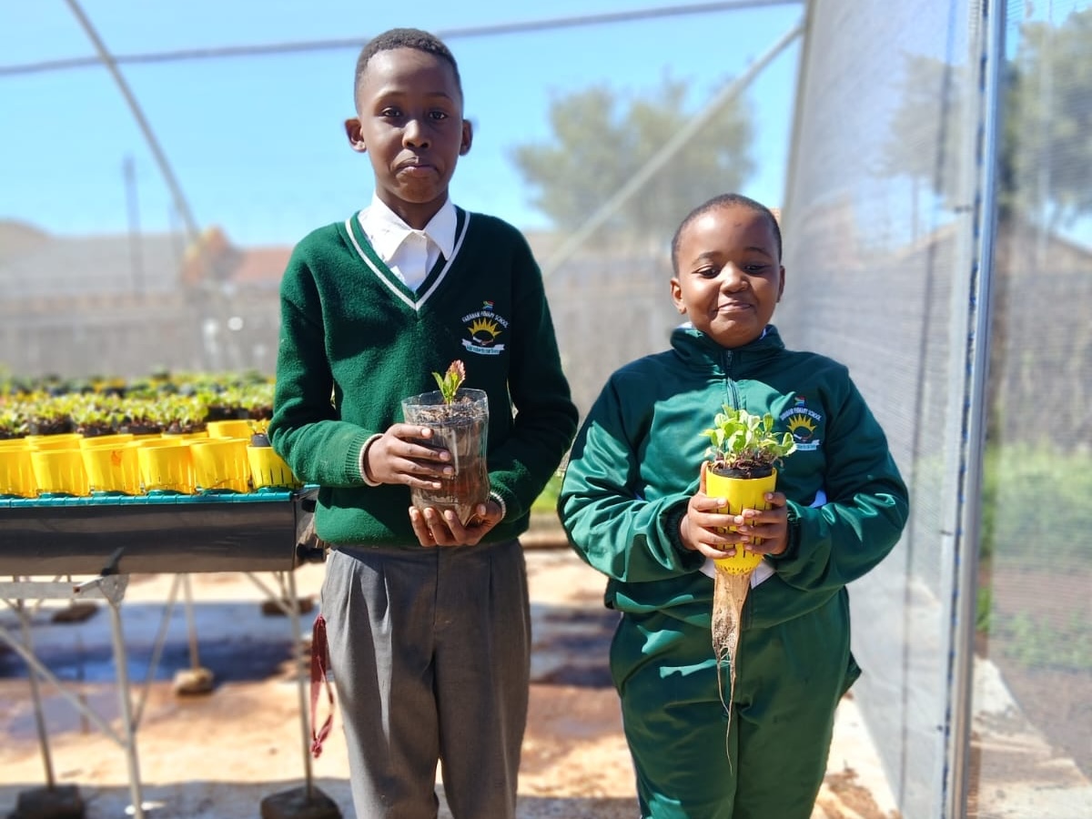 Two schoolchildren proudly holding their own upcycled bottle gardens