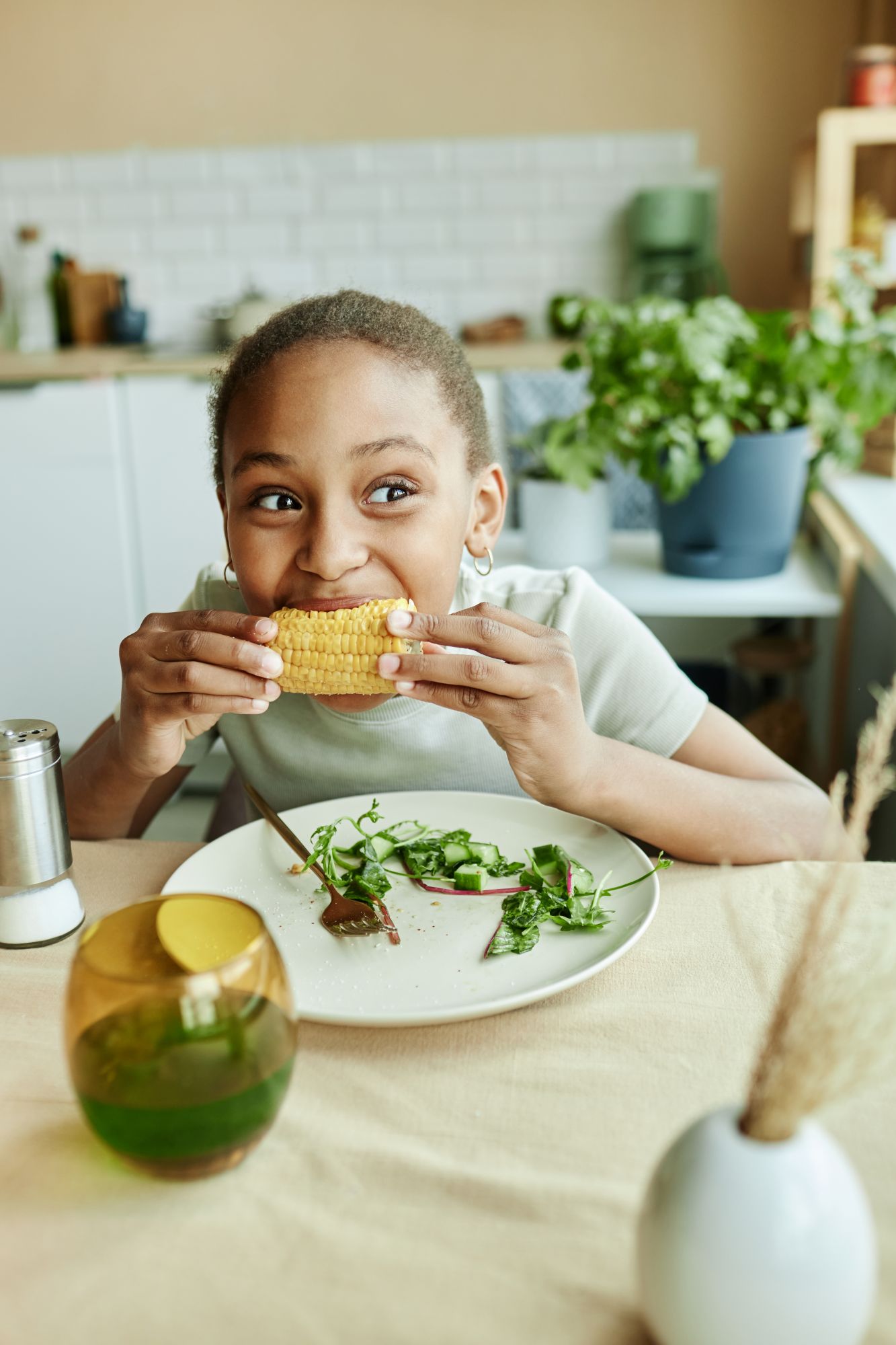 Happy child enjoying fresh corn at the kitchen table